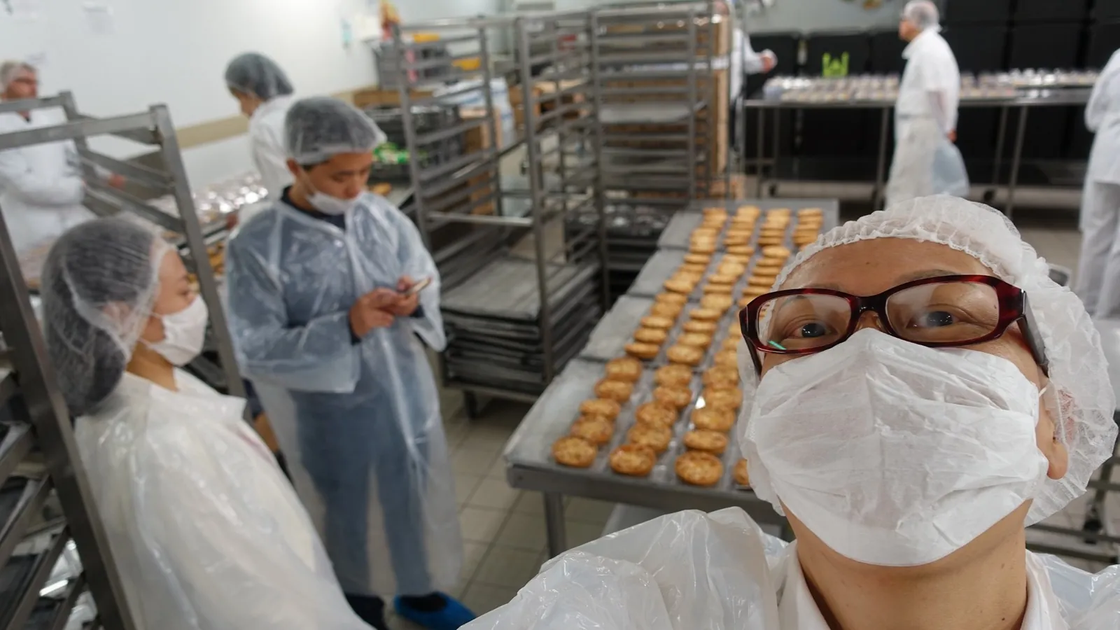 フランスの食品工場で、衛生キャップとマスクを着用し焼き菓子の製造ラインを視察する宮内海。