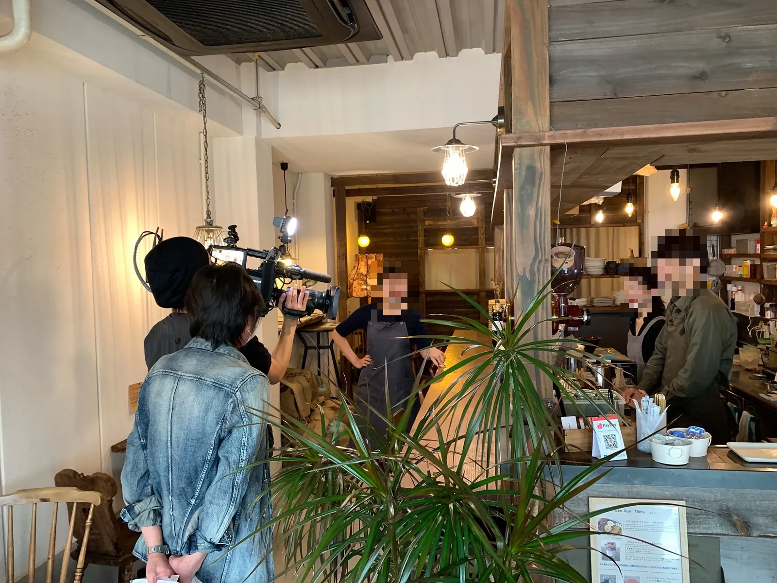カフェの店内で、カメラを担いでスタッフを撮影している動画制作の現場。