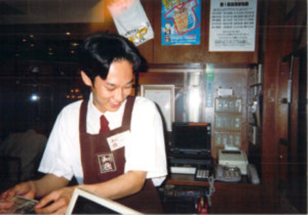 ワタミフードサービス入社当時、店長として店内で笑顔で立つ若き日の宮内海。